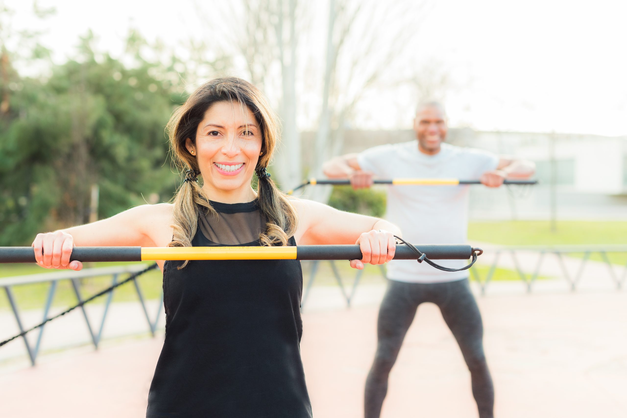 Front view of cheerful fitness couple exercising with an elastic gym stick in the park